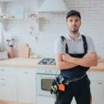 Male technician in modern kitchen, ready for work, representing certified plumbing services and backflow testing.