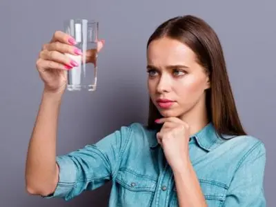 Woman examining a glass of water with a concerned expression, highlighting the importance of clean drinking water and the need for a water filtration system to ensure safety and quality.