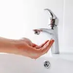 Hand reaching for a chrome faucet with water flowing, emphasizing plumbing service and hygiene.