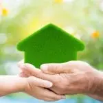 Two hands holding a green house symbol against a warm backdrop, related to Charles Krull & Son plumbing services.