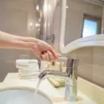 Hand reaching for modern faucet in clean bathroom, promoting water conservation by Charles Krull & Son Plumbing.