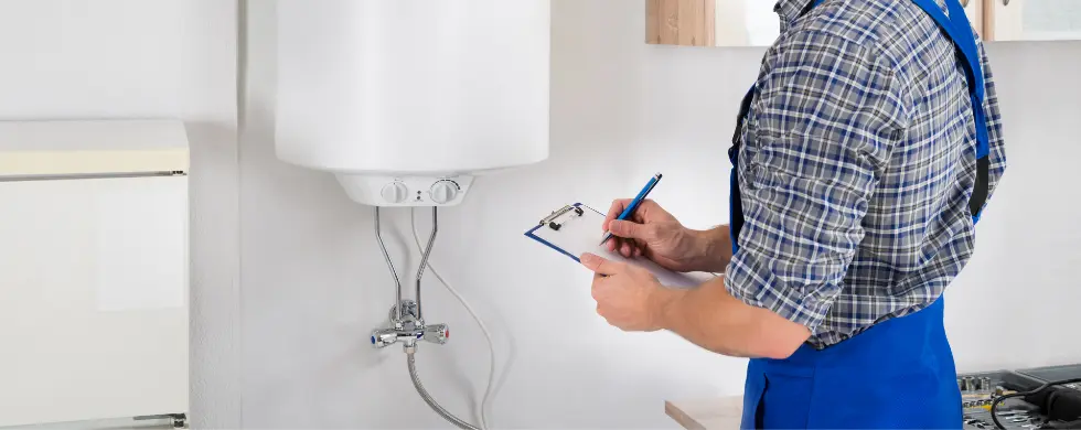 Technician in a blue apron inspecting a white water heater, part of Charles Krull & Son plumbing services.