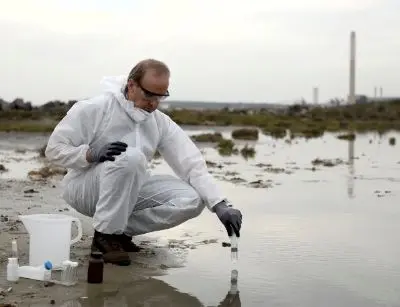 Scientist in protective gear collecting water samples from a polluted area, emphasizing the importance of water filtration systems to remove harmful contaminants.