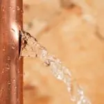 Copper pipe with visible water leak, illustrating the importance of professional plumbing services for leak detection and repair.