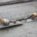 Two hands using a trowel on wet concrete during plumbing work related to slab leaks by Charles Krull & Son, Inc.