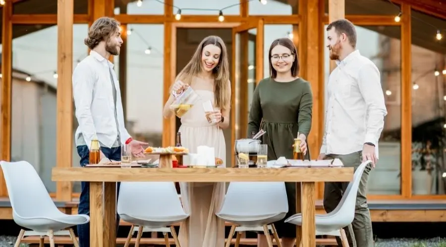 Four friends enjoying food and drinks around a wooden table in a festive outdoor setting, relevant to plumbing updates.