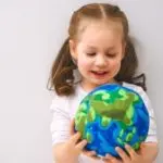 A young girl with two ponytails examines a colorful globe while learning about water conservation and plumbing services.