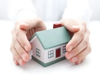 Hands gently cradling a model house, symbolizing home safety and the importance of plumbing maintenance for homeowners.