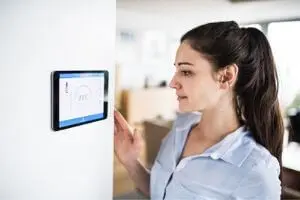Woman adjusting a smart thermostat on a wall, illustrating home temperature control and HVAC system management.