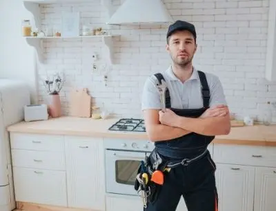 Certified plumber standing confidently in a modern kitchen, equipped with tools, emphasizing the importance of professional backflow testing for safe water supply.