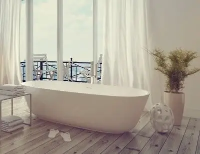 Modern freestanding bathtub in a bright, airy bathroom with wooden flooring, large windows, and a potted plant, emphasizing water conservation benefits over showering.