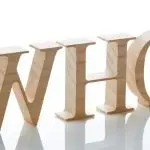 Three-dimensional wooden letters spelling "WHO," representing inquiry and Lillian Baumbach's plumbing legacy.