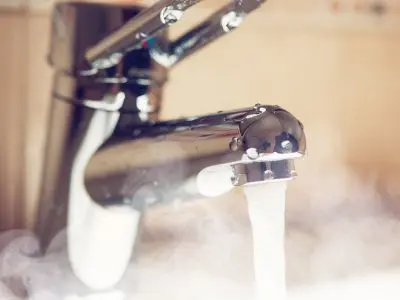Faucet with steaming hot water flowing, illustrating the efficiency and on-demand capabilities of tankless water heaters.
