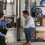 Two technicians discussing a heating system in a garage, emphasizing home maintenance and plumbing services.