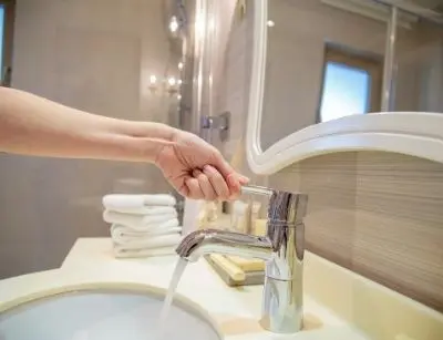 Hand turning off a bathroom faucet, promoting water conservation and eco-friendly practices at home.
