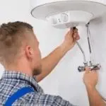 Male technician repairing a water heater with tools, demonstrating plumbing services by Charles Krull & Son, Inc.