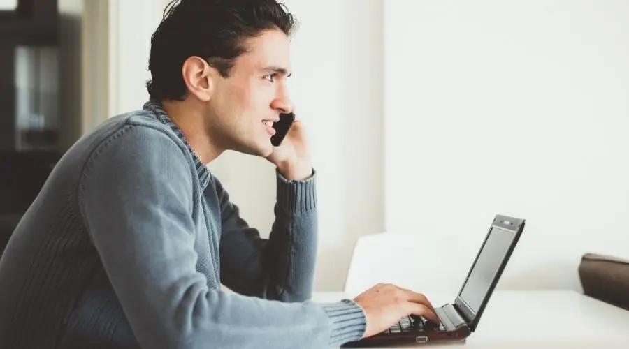 Young man in casual setting, on mobile phone with laptop, working in plumbing and heating service context.