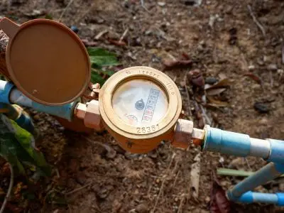 Water meter with open lid, displaying reading, surrounded by dirt and foliage, illustrating leak detection methods for homeowners.
