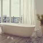 Freestanding bathtub in a modern bathroom with sheer curtains and a scenic window view, highlighting water conservation tips.