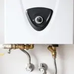 White wall-mounted water heater with control knob and pipes, representing plumbing services by Charles Krull & Son, Inc.