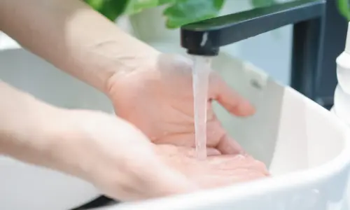 Hands cupping water from a faucet, demonstrating the practice of letting water run at a drip to prevent frozen pipes.