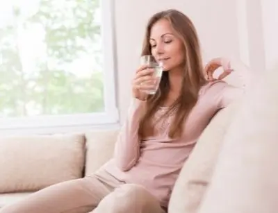Woman enjoying a glass of clean water indoors, promoting health benefits of filtered water for detoxification and hydration.