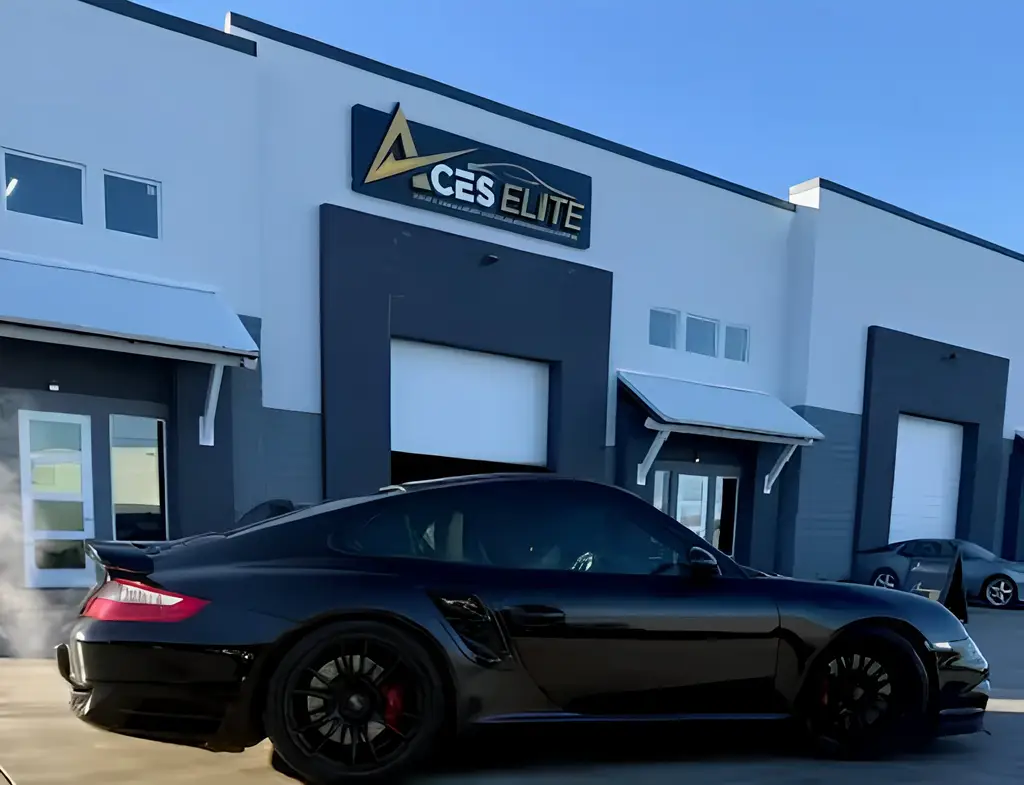 Aces Auto Elite - A black sports car is parked in front of a modern industrial building with a sign reading ACES ELITE SERVICE above the entrance on a clear day. | Arizona Luxury & Exotic Car Service