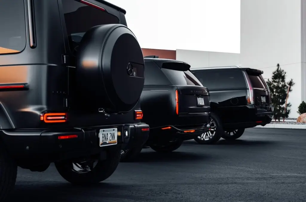 Aces Auto Elite - Three black luxury SUVs are parked side by side on a paved lot near a modern building, showing their stylish rear designs and license plates. | Arizona Luxury & Exotic Car Service