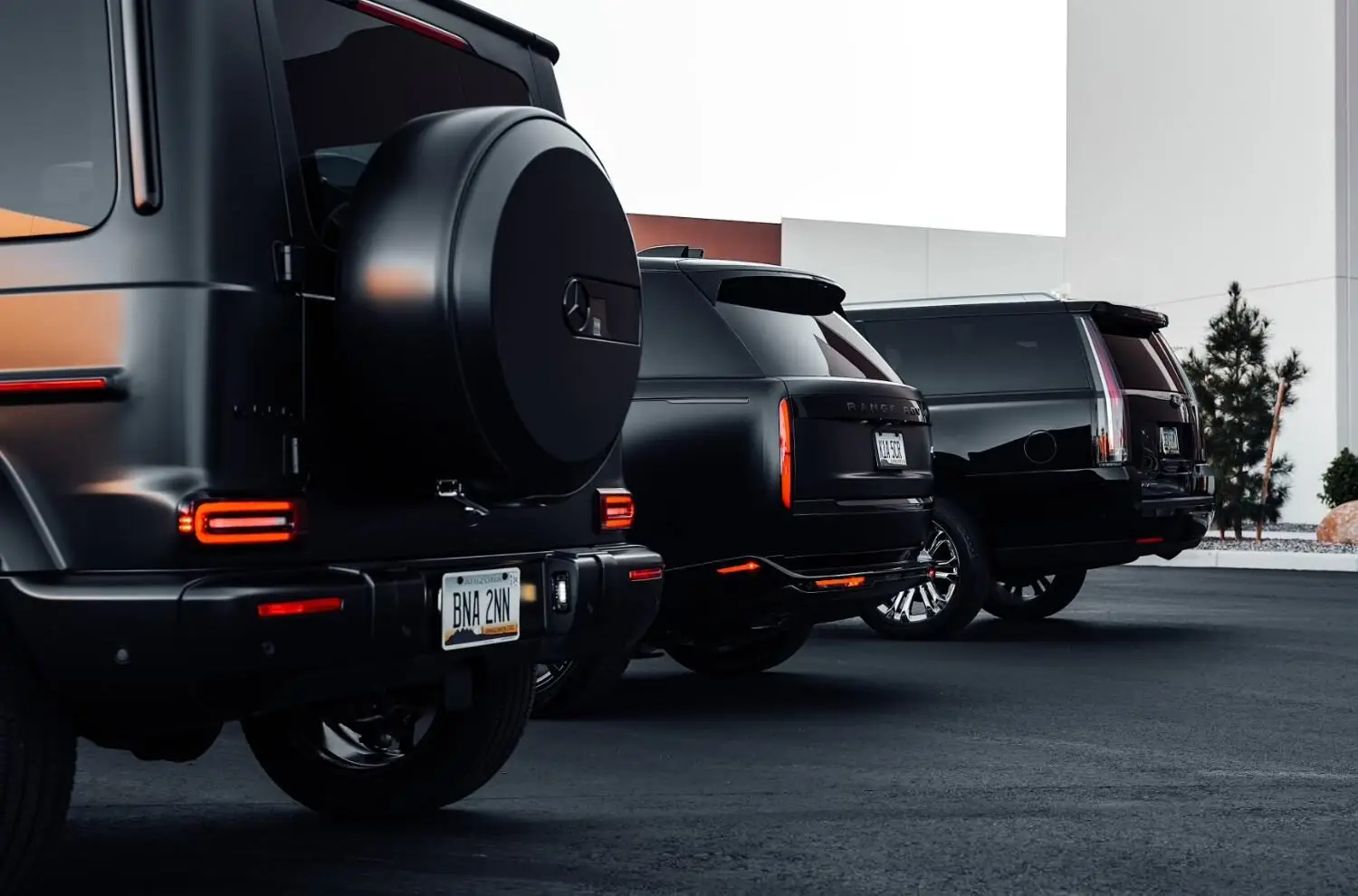 Aces Auto Elite - Three black luxury SUVs are parked side by side on a paved lot near a modern building, showing their stylish rear designs and license plates. | Arizona Luxury & Exotic Car Service