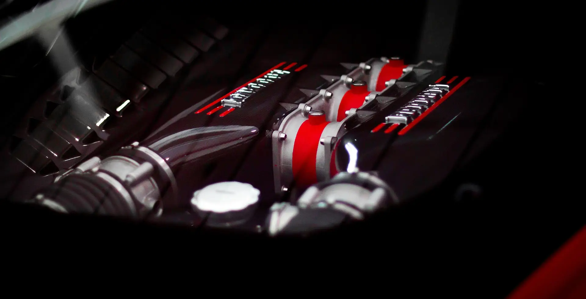 Aces Auto Elite - Close-up view of a Ferrari engine with red and black components, metallic details, and the Ferrari logo visible, set against a dark background. | Arizona Luxury & Exotic Car Service