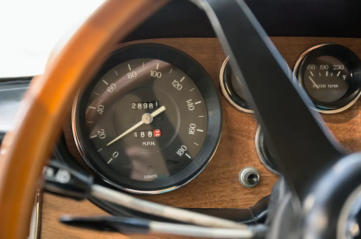 Aces Auto Elite - Close-up of a classic car dashboard highlights the preservation of a vintage speedometer with a wooden panel. The needle points to 33 MPH, odometer reads 28,981 miles, and part of the steering wheel and other gauges reflect careful restoration. | Arizona Luxury & Exotic Car Service