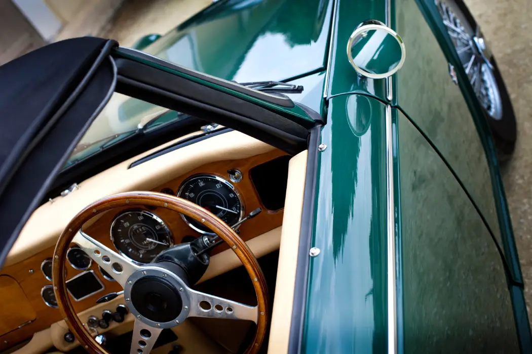 Aces Auto Elite - Close-up of a classic green convertible car, showcasing its wooden steering wheel, vintage dashboard gauges, and shiny side mirror—an impressive example of restoration with part of the black soft top and chrome wheels also visible. | Arizona Luxury & Exotic Car Service