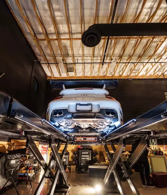 Aces Auto Elite - A white sports car is elevated on a lift in a modern, well-lit auto repair shop, revealing its undercarriage and exhaust system. Tools and equipment are visible around the workspace. | Arizona Luxury & Exotic Car Service