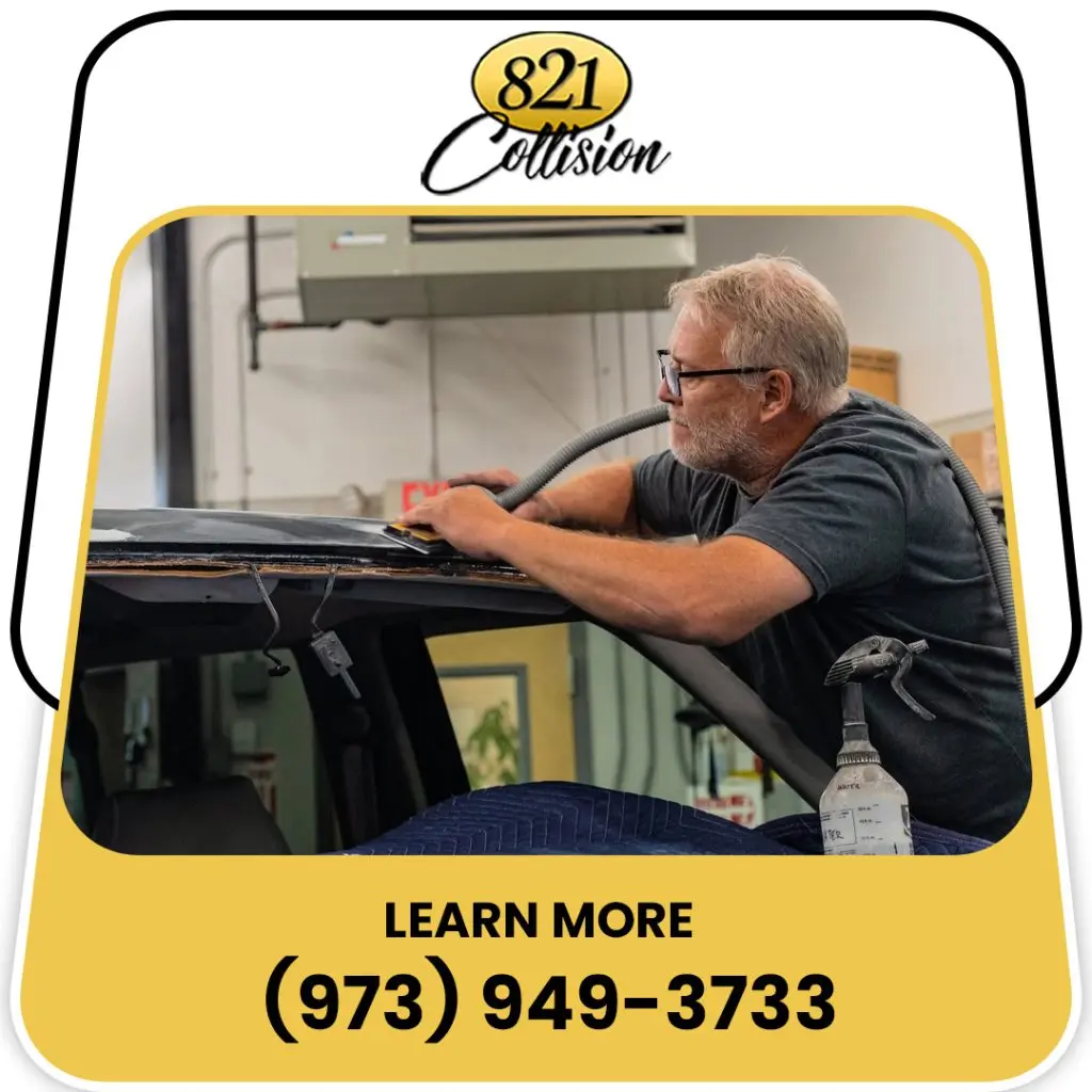 An auto body technician carefully hand sanding and prepping the windshield frame and roof line of a vehicle in a collision repair shop.