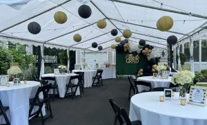 Graduation party setup inside a large outdoor event tent with tables, balloons, and decorations