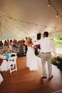 Wedding couple dancing on a wood dance floor under a large event tent with string lights and guests