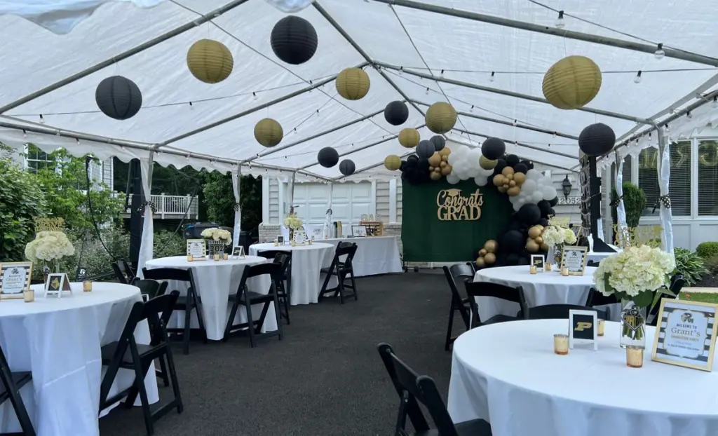 Graduation party setup inside a large outdoor event tent with tables, balloons, and decorations