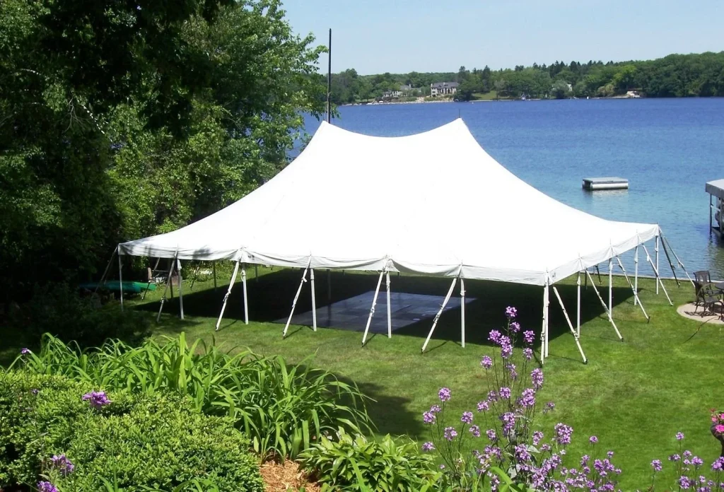 Large white party tent set up on green grass by a lake, surrounded by blooming flowers, ideal for outdoor spring events.