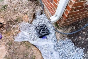 Basement waterproofing system failure showing a clogged exterior drainage basin and downspout drainage near a home's foundation.