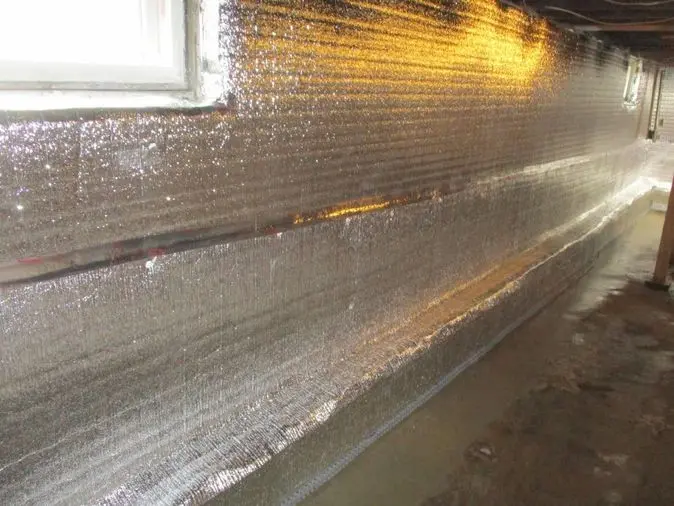 Basement interior with reflective waterproofing material applied to walls, showcasing Aqua Dry Basement Waterproofing's services in the Hopewell area.