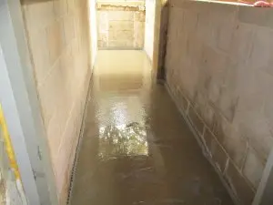 Flooded basement corridor with standing water, showcasing the need for effective sump pump installation and waterproofing solutions.