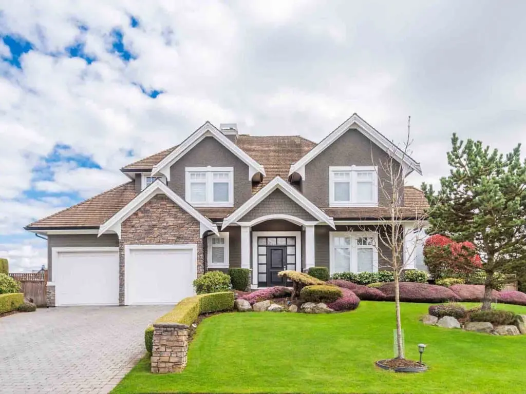 Beautifully landscaped residential home with a modern design, featuring a stone and gray exterior, two-car garage, manicured lawn, and decorative shrubs, illustrating quality and attention to detail in property maintenance.