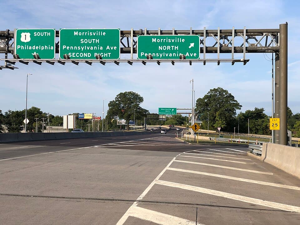 Road signs indicating directions to Morrisville, PA, with exits for South Pennsylvania Ave and North Pennsylvania Ave, featuring clear blue skies and green trees in the background.