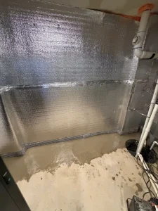 Completed basement waterproofing system in Cranbury, NJ featuring reflective wall insulation, interior French drain, drainage board, and freshly poured concrete.