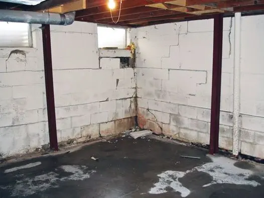 Basement foundation wall with horizontal and vertical cracks, water damage, and signs of structural pressure in a residential home