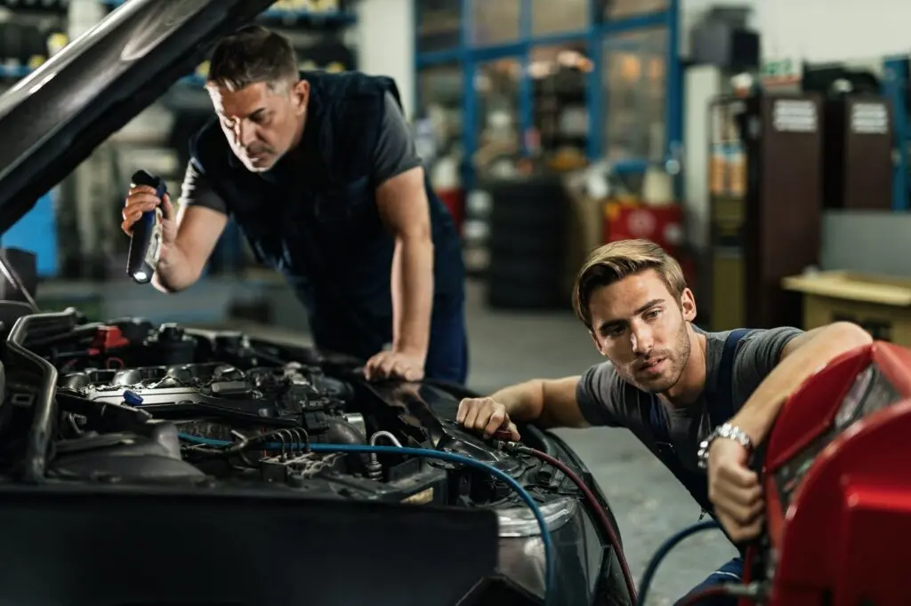 Two mechanics repairing air conditioning system in auto repair shop.