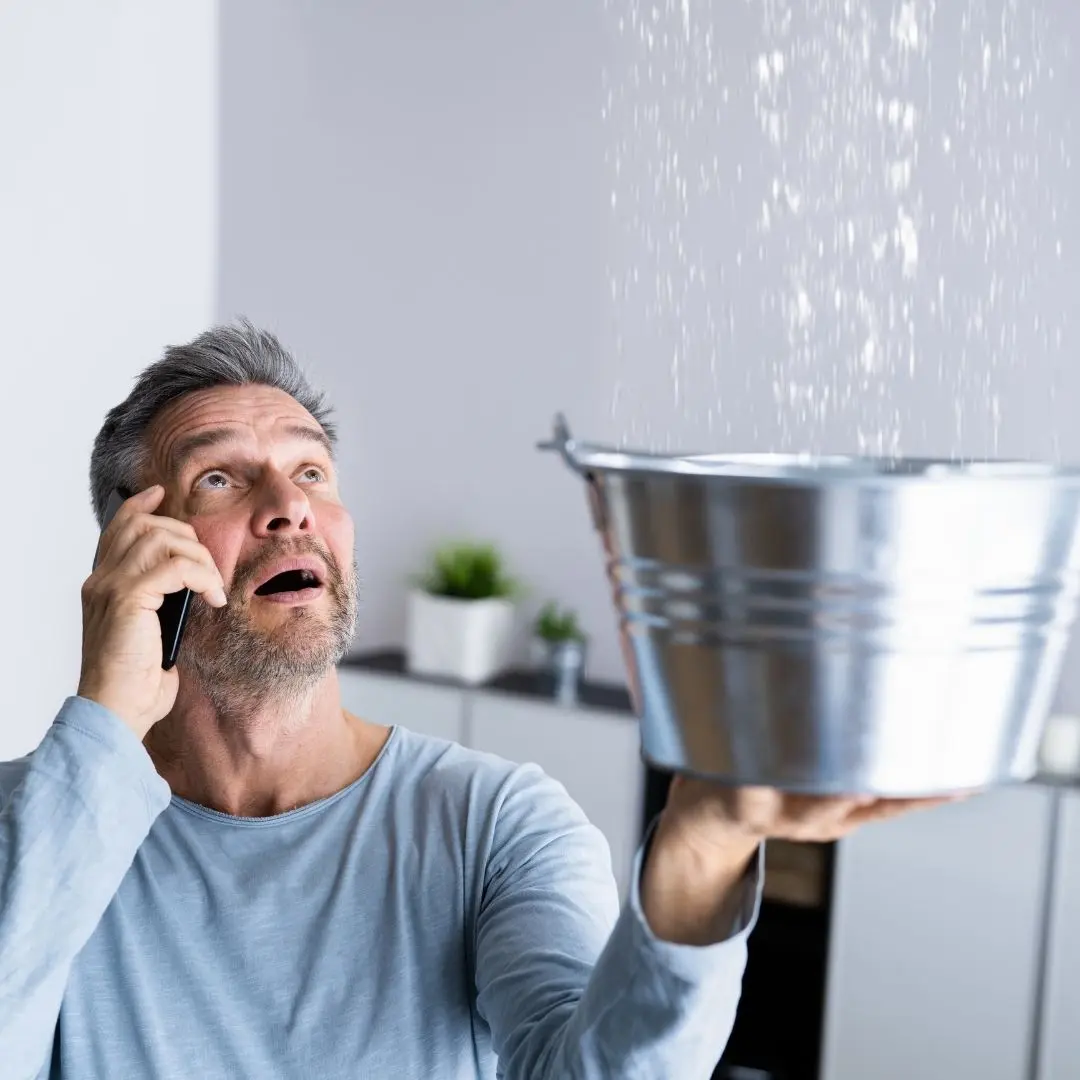 older-gentleman-on-phone-holding-bucket-collecting-water-leak