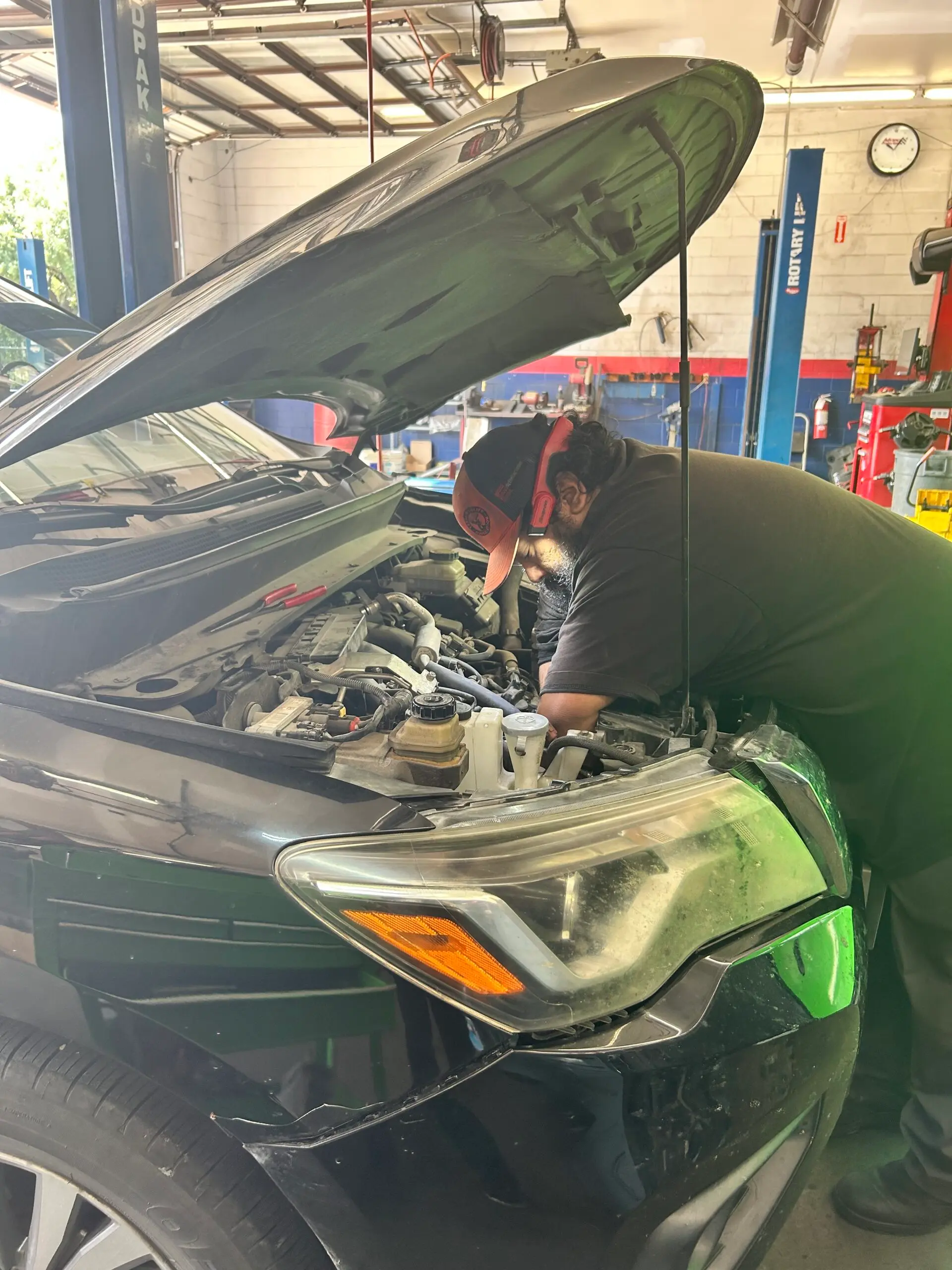 Technician performing under-hood inspection for summer car maintenance in Houston