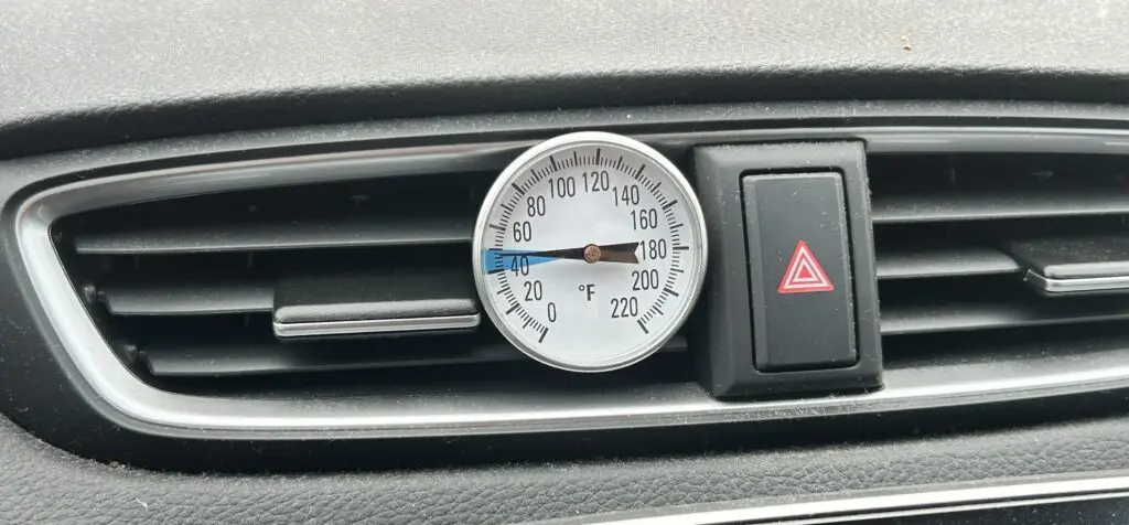 Measuring car AC vent temperature during summer inspection in Houston