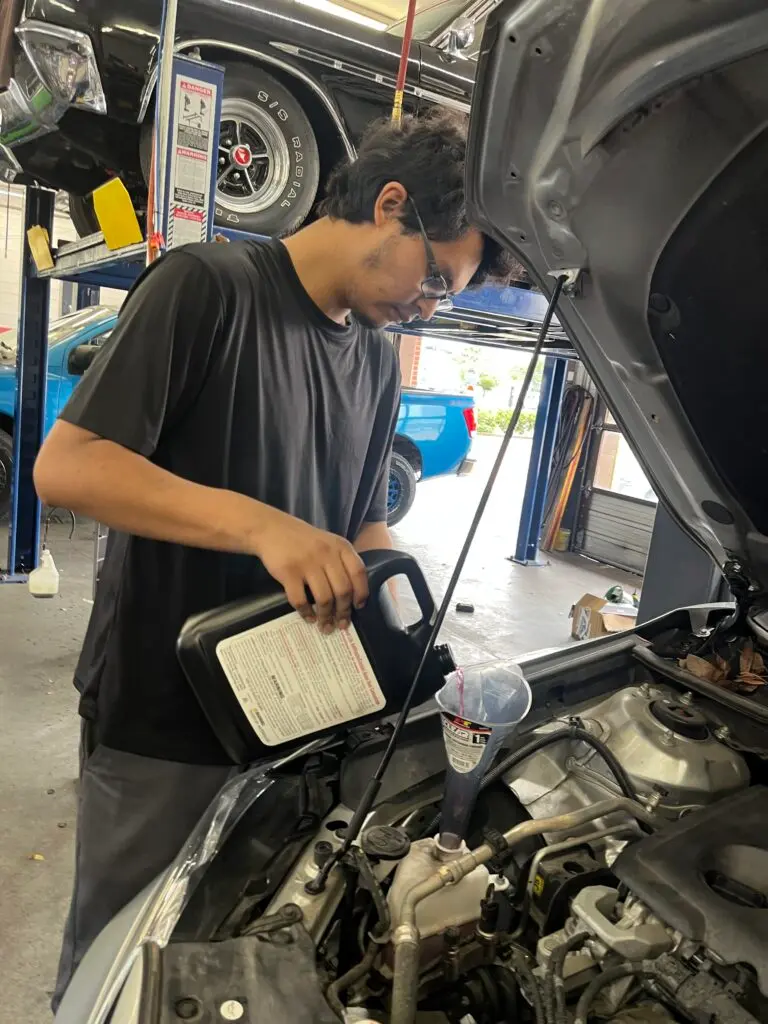 Technician checking and topping off engine coolant during vehicle maintenance.